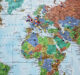 A paper world map hanging on a wall dotted with colorful pins marking destinations